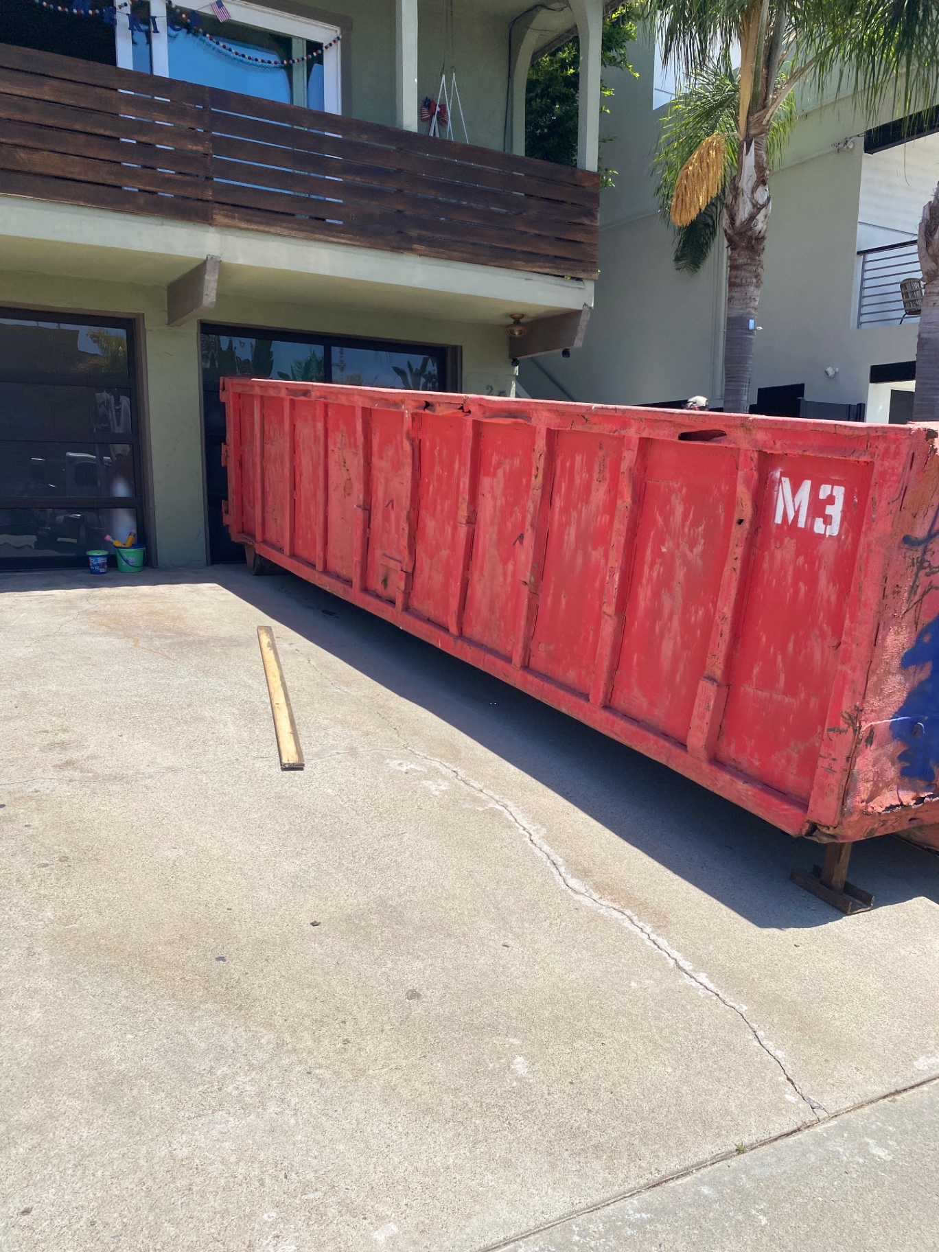 Large red roll-off dumpster on the driveway of an Ocean Beach two-story home during a remodel
