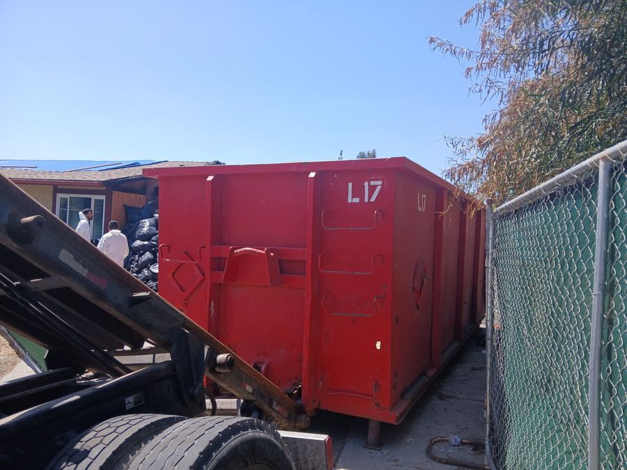 Heverly & Sons crew loading a full red roll-off dumpster during a San Diego home cleanout