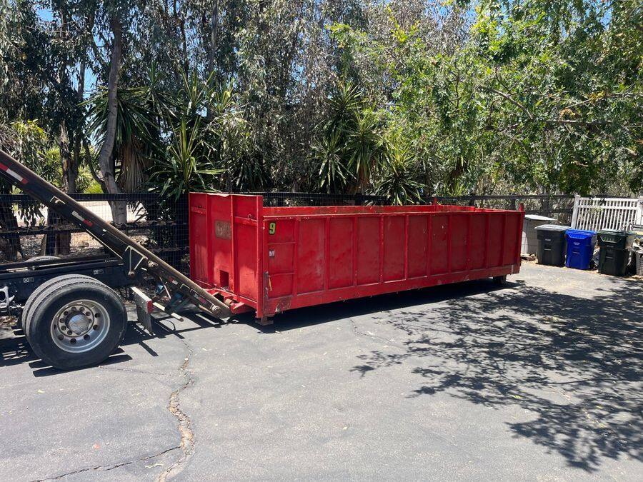 20-yard red roll-off dumpster placed on a North County driveway under eucalyptus trees