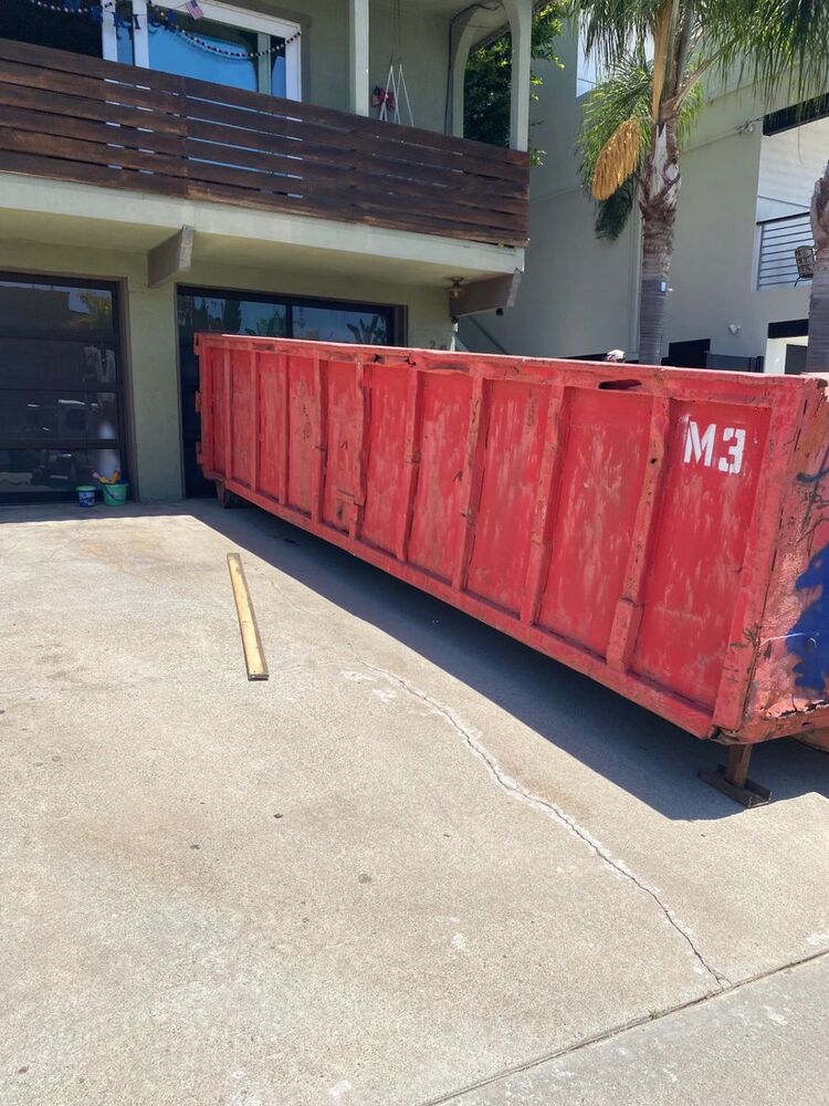 Red 20-yard roll-off dumpster on a Pacific Beach driveway for a full house cleanout